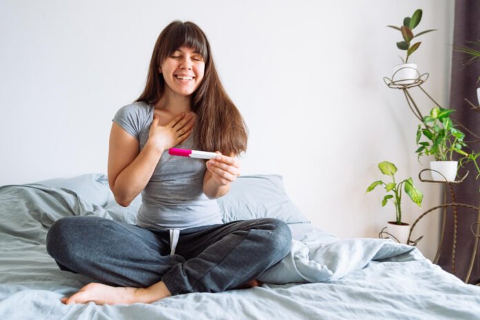young happy woman sitting bed looking positive pregnancy test